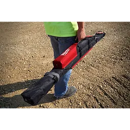 Person carrying the Milwaukee REDSTICK Starter Set in a rugged black and red case on a gravel surface.