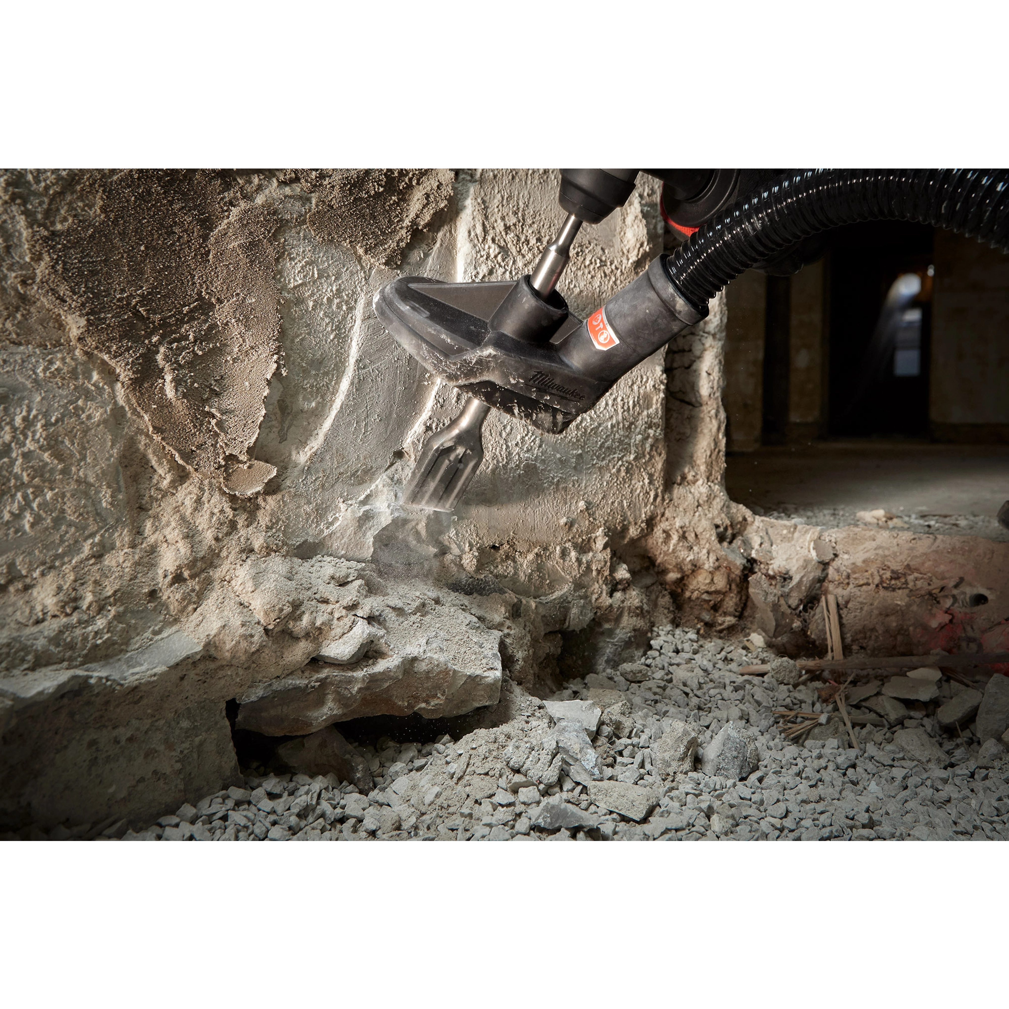 SDS%2B%201-1%2F2%22%20SCALING tool in use, chipping away at a concrete wall with an attached vacuum hose collecting dust.