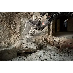 SDS%2B%201-1%2F2%22%20SCALING tool in use, chipping away at a concrete wall with an attached vacuum hose collecting dust.
