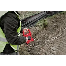 A person holds a Milwaukee 100 Foot Fiberglass Long Tape at a construction site, preparing to measure the ground.