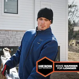 A person wears a blue M12 Heated TOUGHSHELL Jacket while carrying a ladder outdoors. The text reads "HEXON Heat Technology: Stays Warmer for Longer."