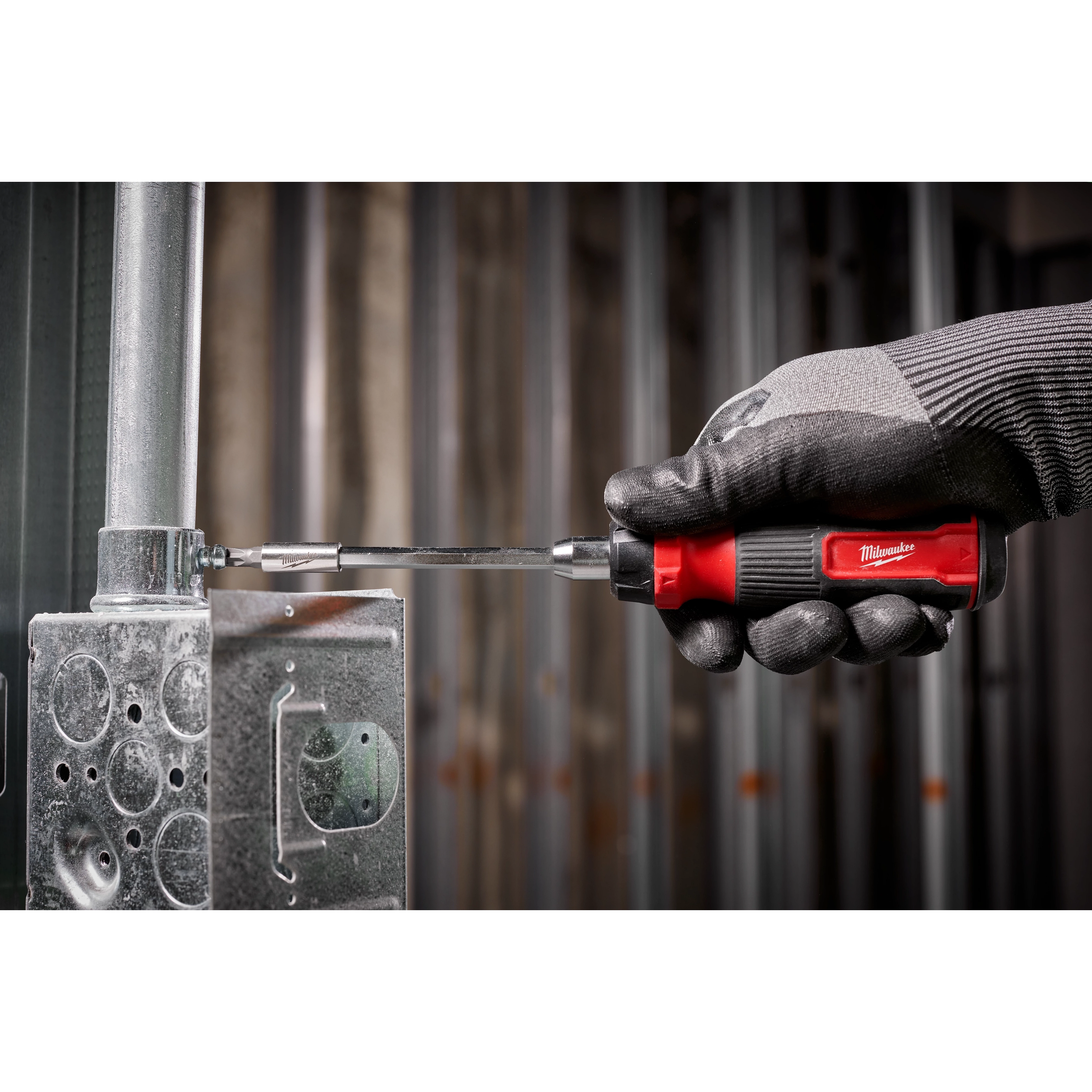 A gloved hand uses the 14-in-1 Ratcheting Multi-Bit Screwdriver to tighten a screw on a metallic industrial component.