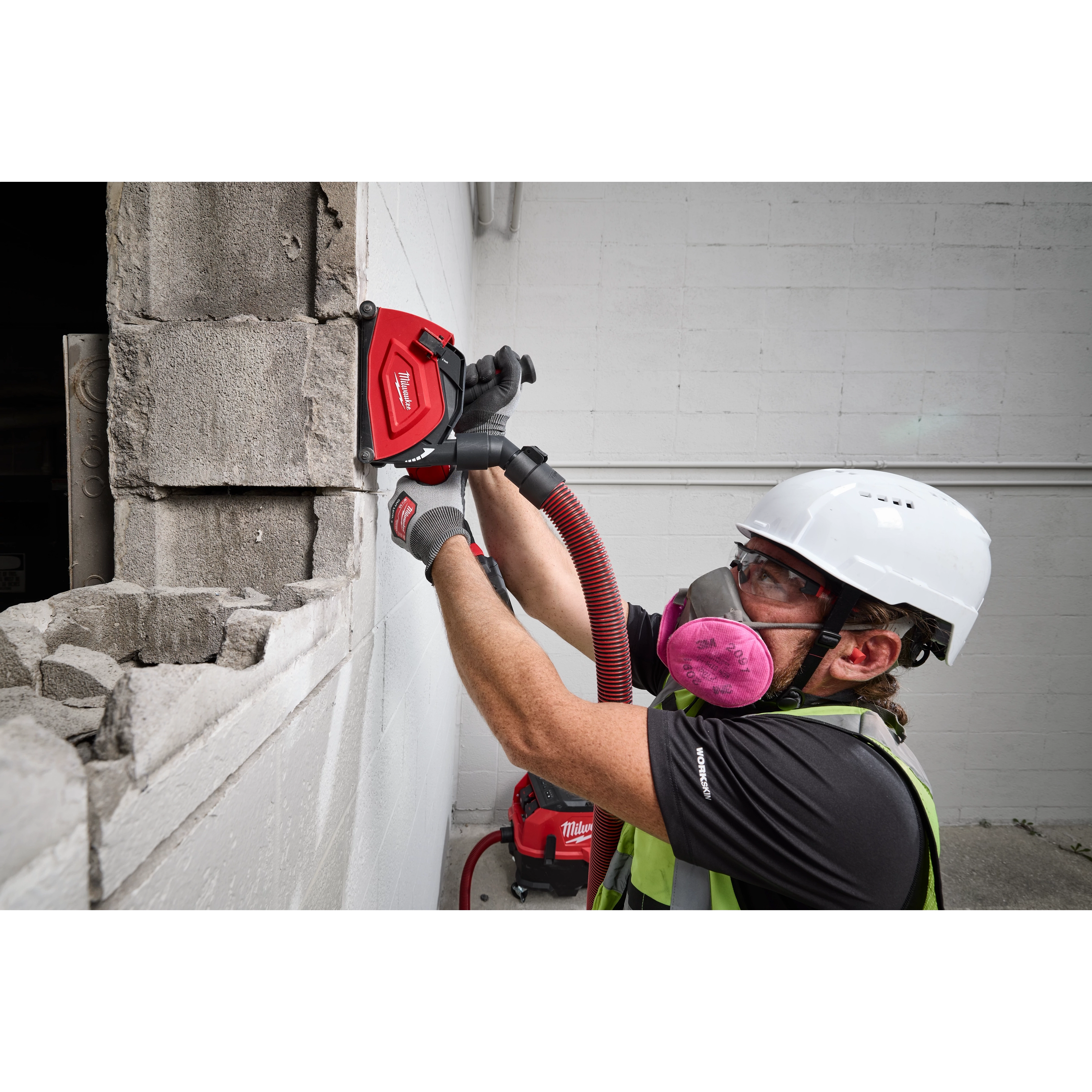 A construction worker uses a Milwaukee 5" Cutting Dust Shroud on concrete blocks. The shroud is attached to a vacuum system to minimize dust while cutting.