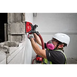 A construction worker uses a Milwaukee 5" Cutting Dust Shroud on concrete blocks. The shroud is attached to a vacuum system to minimize dust while cutting.