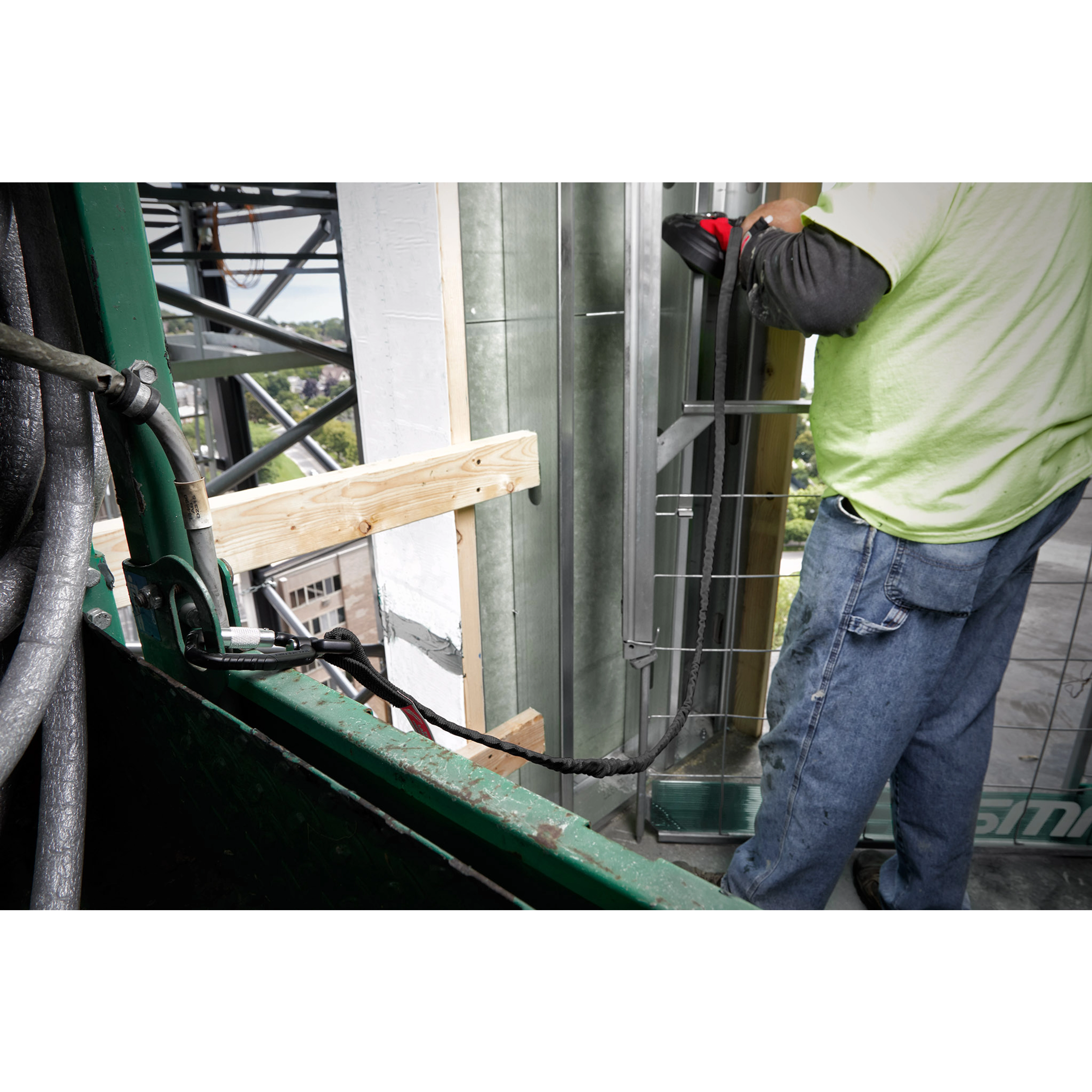 Construction worker using a 15LBS 72" Extended Reach Locking Tool Lanyard, secured to a basket while working on a high-rise structure.