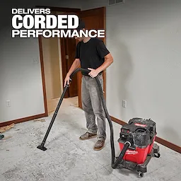 A person using the M18 FUEL™ NEXUS™ 6 Gallon Wet/Dry Vacuum to clean debris from a floor. Text overlay reads "Delivers Corded Performance" in large font. The vacuum is red with black accents and is being used in a residential room.