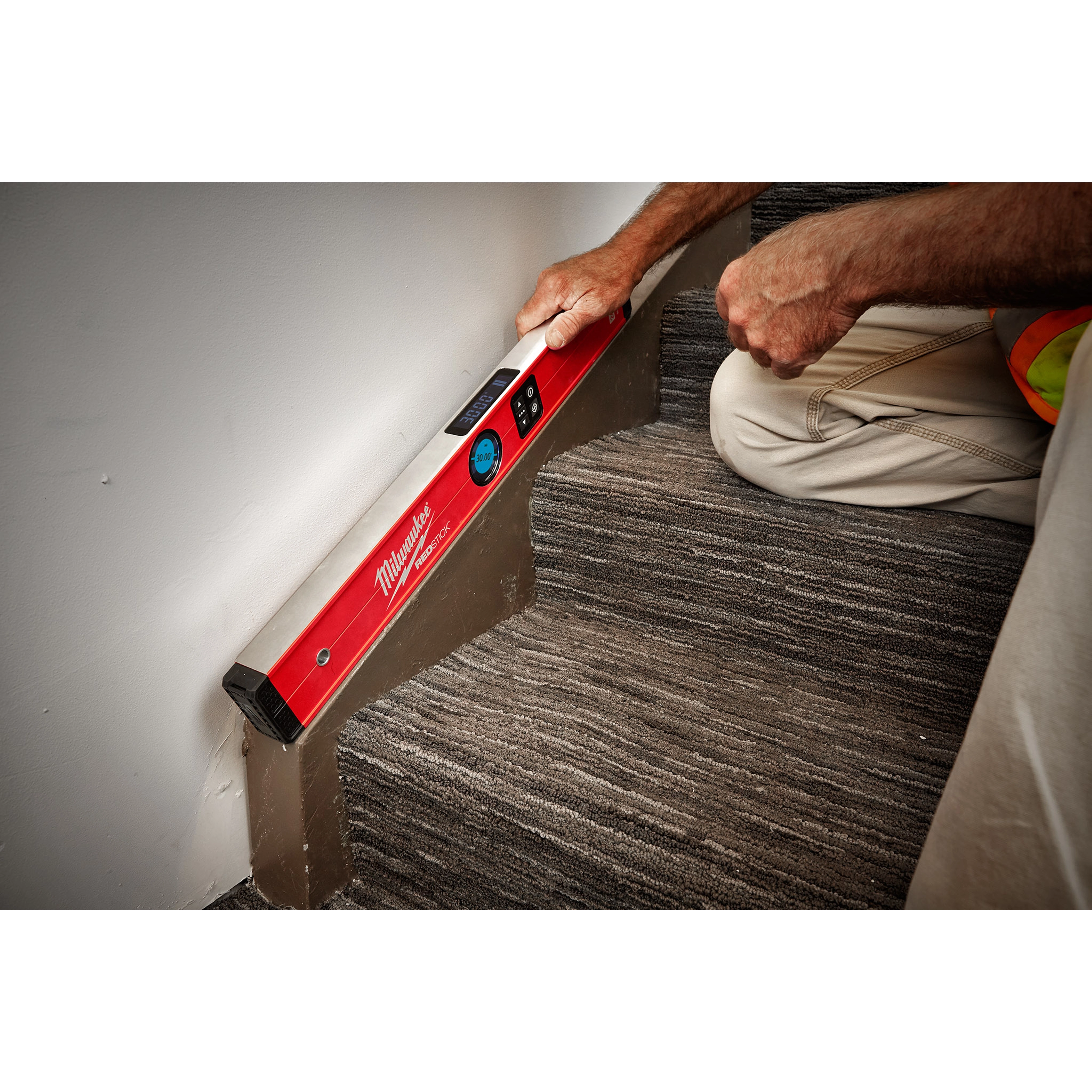 A Milwaukee REDSTICK Digital Level with PINPOINT Measurement Technology is being used by a person to check the angle of a stair step.