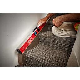 A Milwaukee REDSTICK Digital Level with PINPOINT Measurement Technology is being used by a person to check the angle of a stair step.