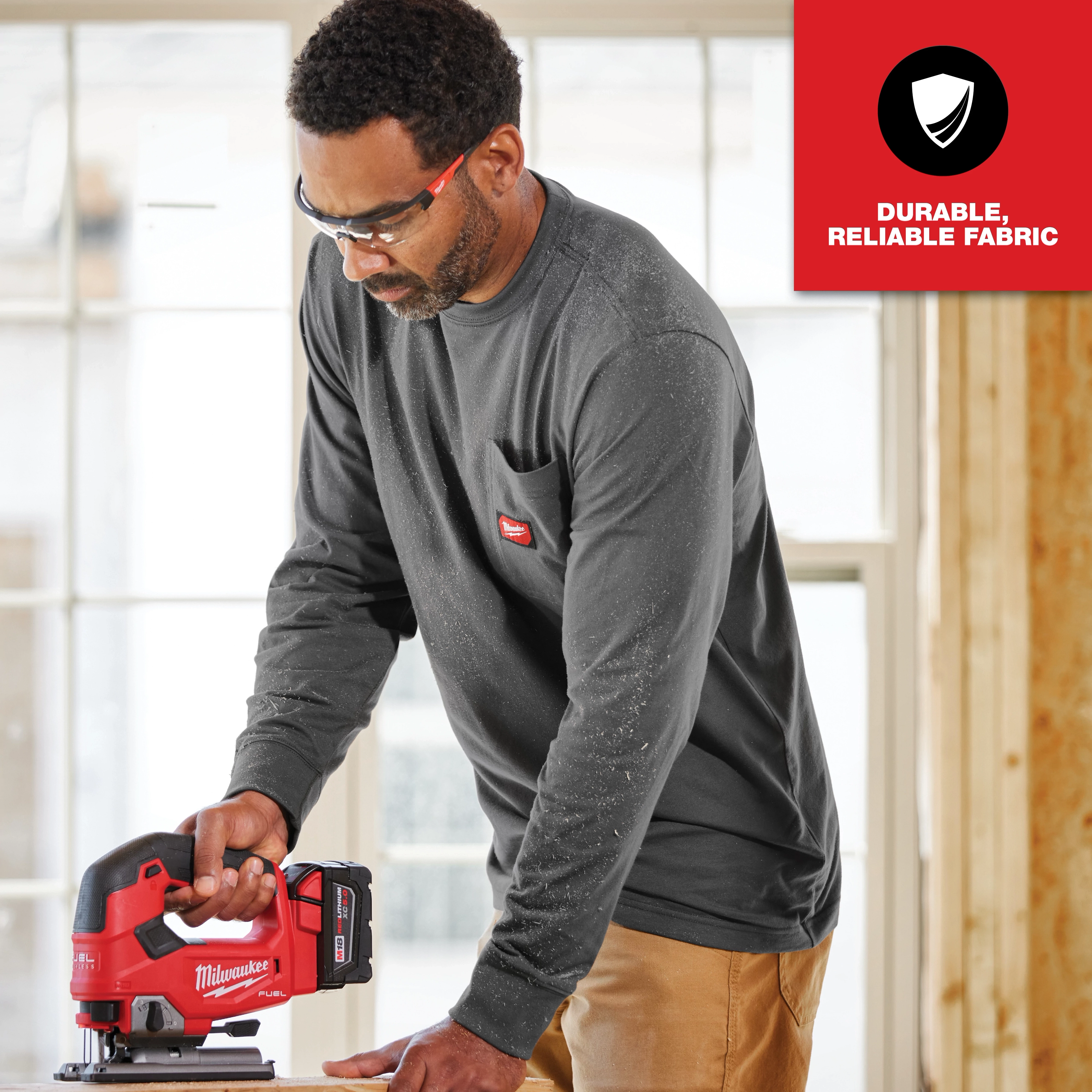 Man wearing GRIDIRON Pocket T-Shirt - Long Sleeve, in a workshop setting using a red power tool. Text: Durable, Reliable Fabric.