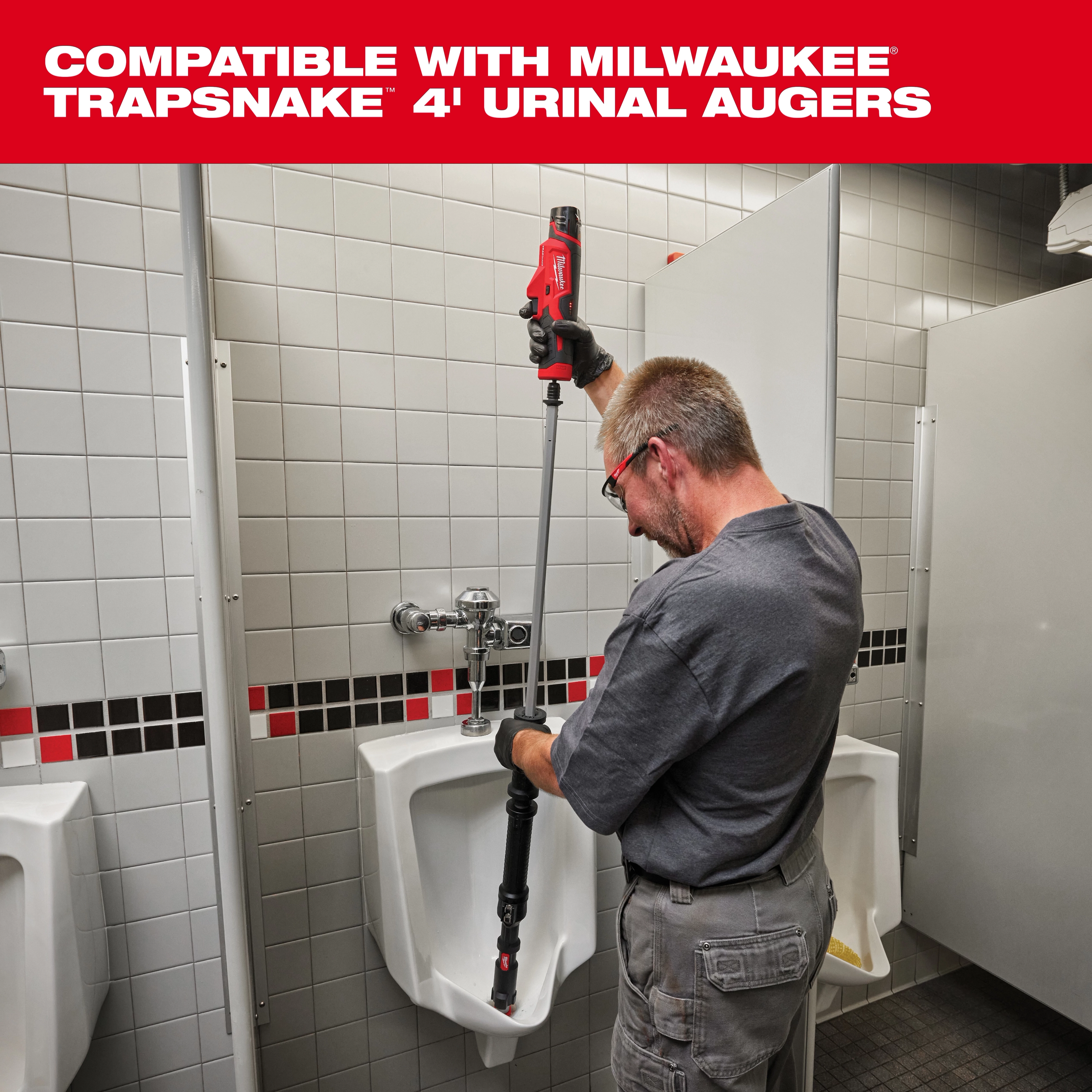 A man uses a Milwaukee TRAPSNAKE 4' Urinal Auger to clear a urinal in a tiled restroom. The product is a plumbing tool featuring a red handle and compatible design for efficiently unclogging urinals. The surrounding environment is a restroom with white tiles and black-and-red accents.