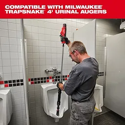 A man uses a Milwaukee TRAPSNAKE 4' Urinal Auger to clear a urinal in a tiled restroom. The product is a plumbing tool featuring a red handle and compatible design for efficiently unclogging urinals. The surrounding environment is a restroom with white tiles and black-and-red accents.