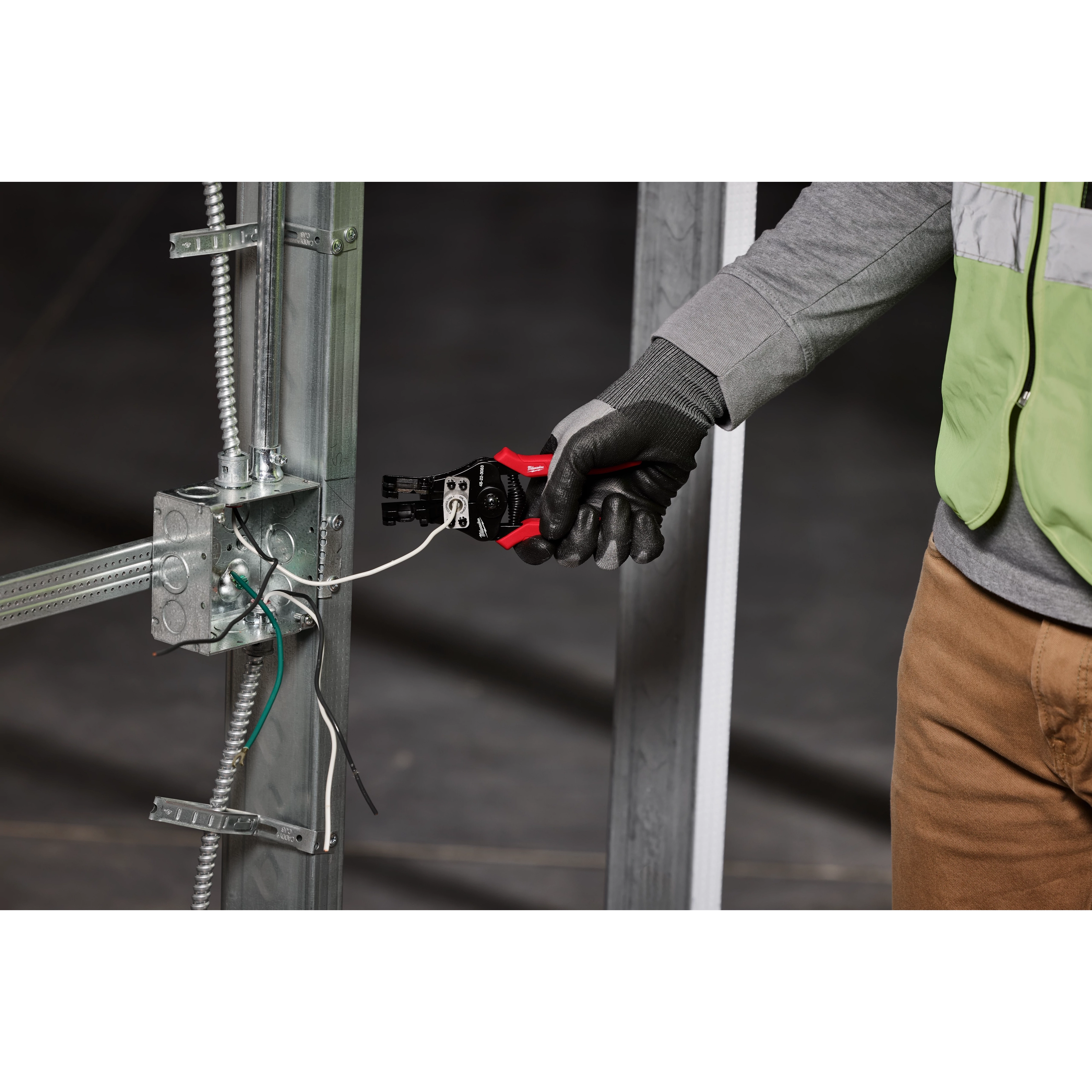 A person wearing gloves uses an Automatic Wire Stripper & Cutter to strip and cut wires attached to a metal frame.