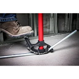 A worker bends a metal conduit using a 1/2 EMT Iron Conduit Bender with a red handle. The foot pressing down aids the bending process.
