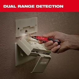 A hand uses the Milwaukee Dual Range Detection tool to test wires in a wall outlet box. The red pen-shaped tool has indicators for detecting voltage in the wires. A caption above reads "DUAL RANGE DETECTION" in white text on a red background.