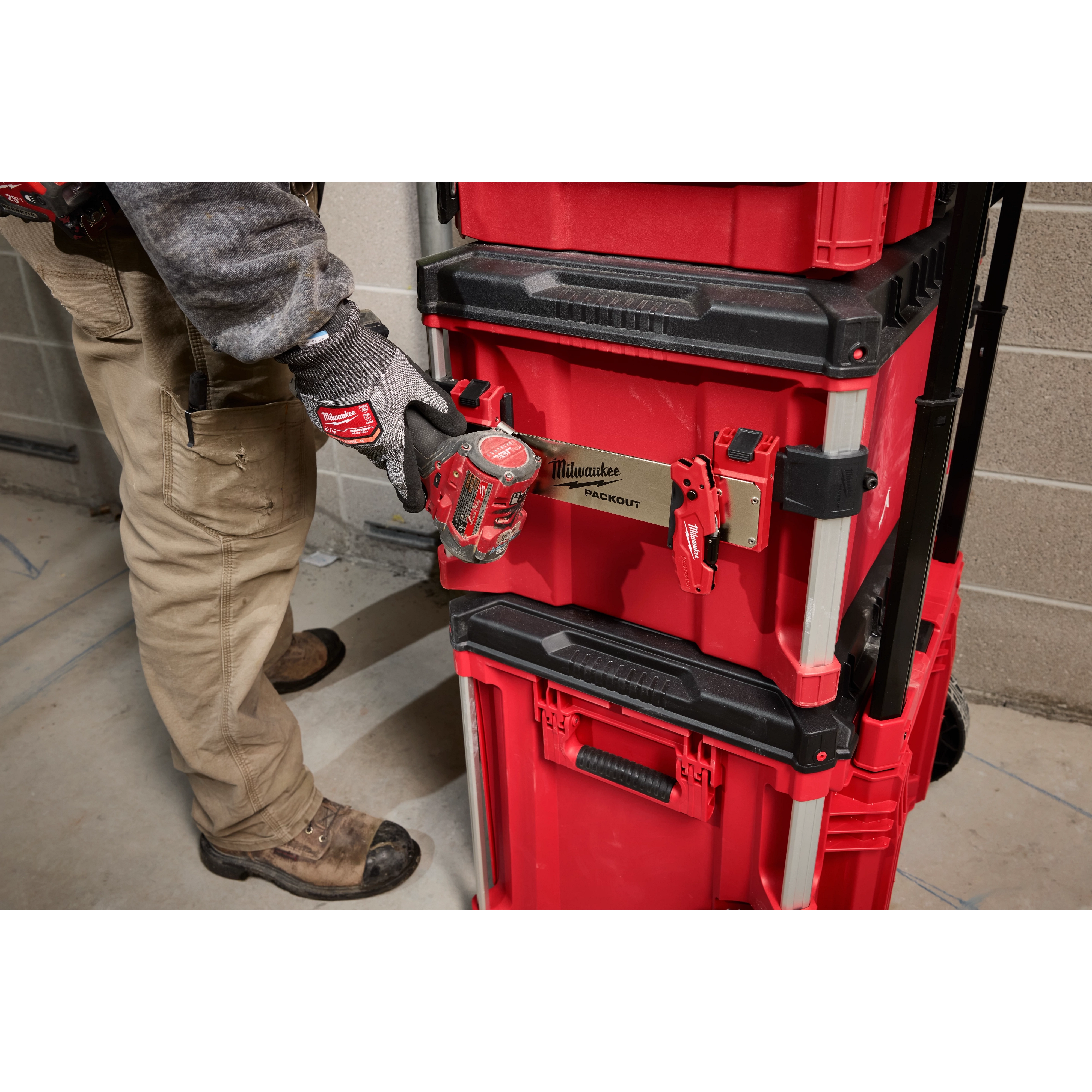 Person attaching a tool to a PACKOUT Tool Box Belt Clip Rack Attachment on a stack of red and black toolboxes.