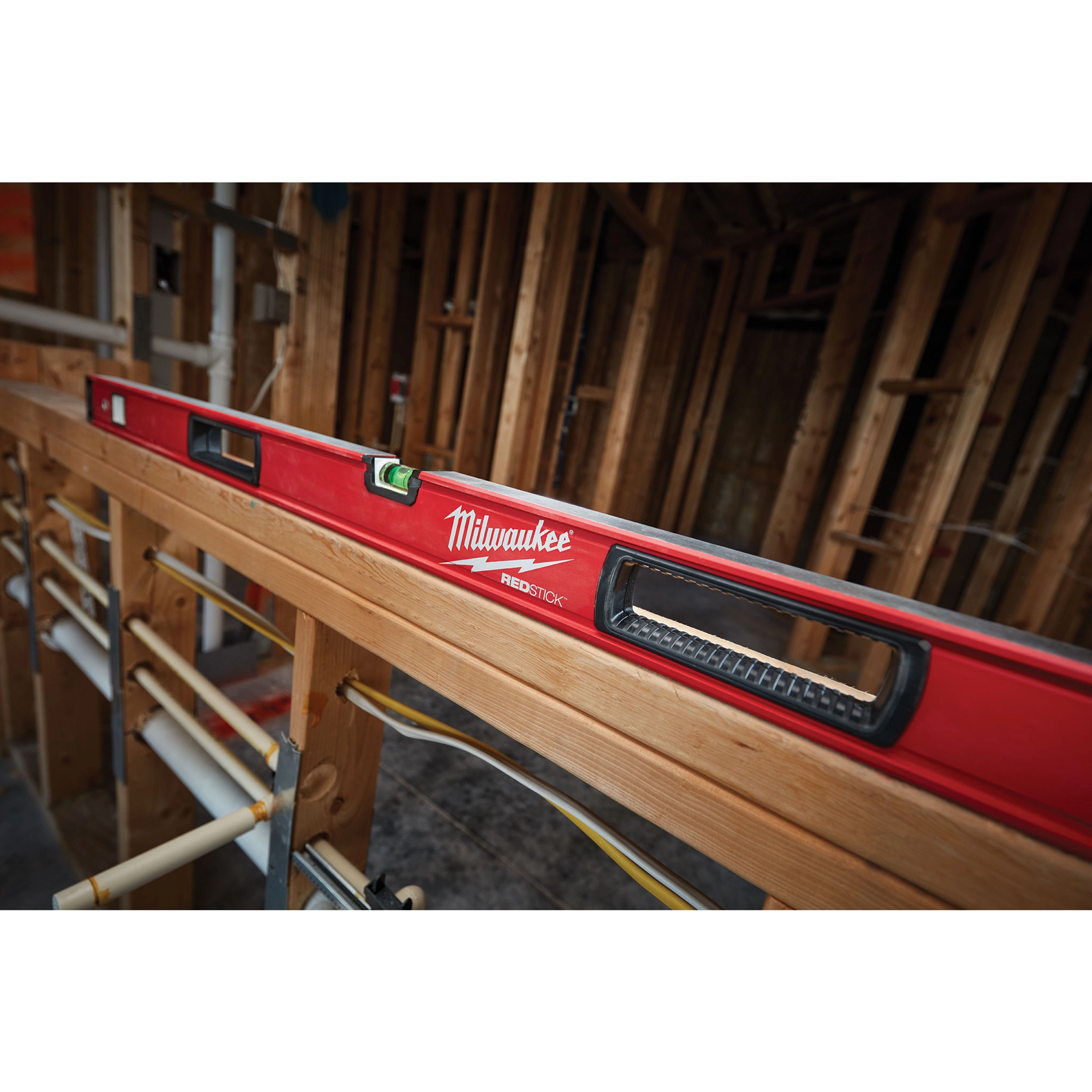 Milwaukee REDSTICK Level on wooden framing in a construction site, displaying its red body and built-in bubble vials for leveling.
