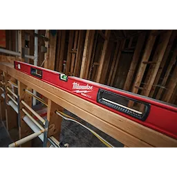 Milwaukee REDSTICK Level on wooden framing in a construction site, displaying its red body and built-in bubble vials for leveling.