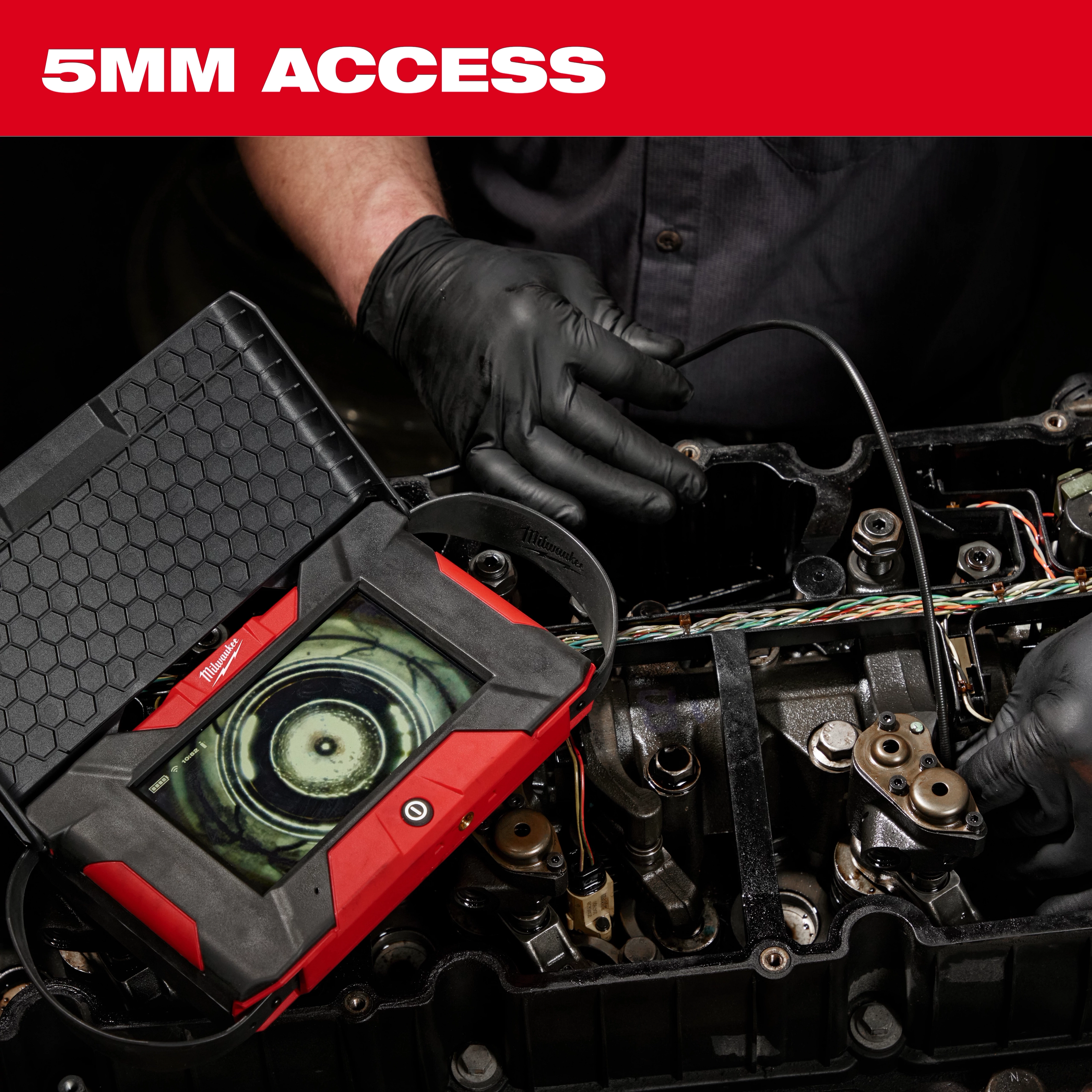 A mechanic uses the M12™ Auto Shop Borescope with Wi-Fi® File Sharing to inspect an engine. The borescope screen shows detailed internal components, aiding in diagnostics and repair. The product is designed for 5mm access, perfect for tight spaces. The mechanic wears black gloves and uses various tools.