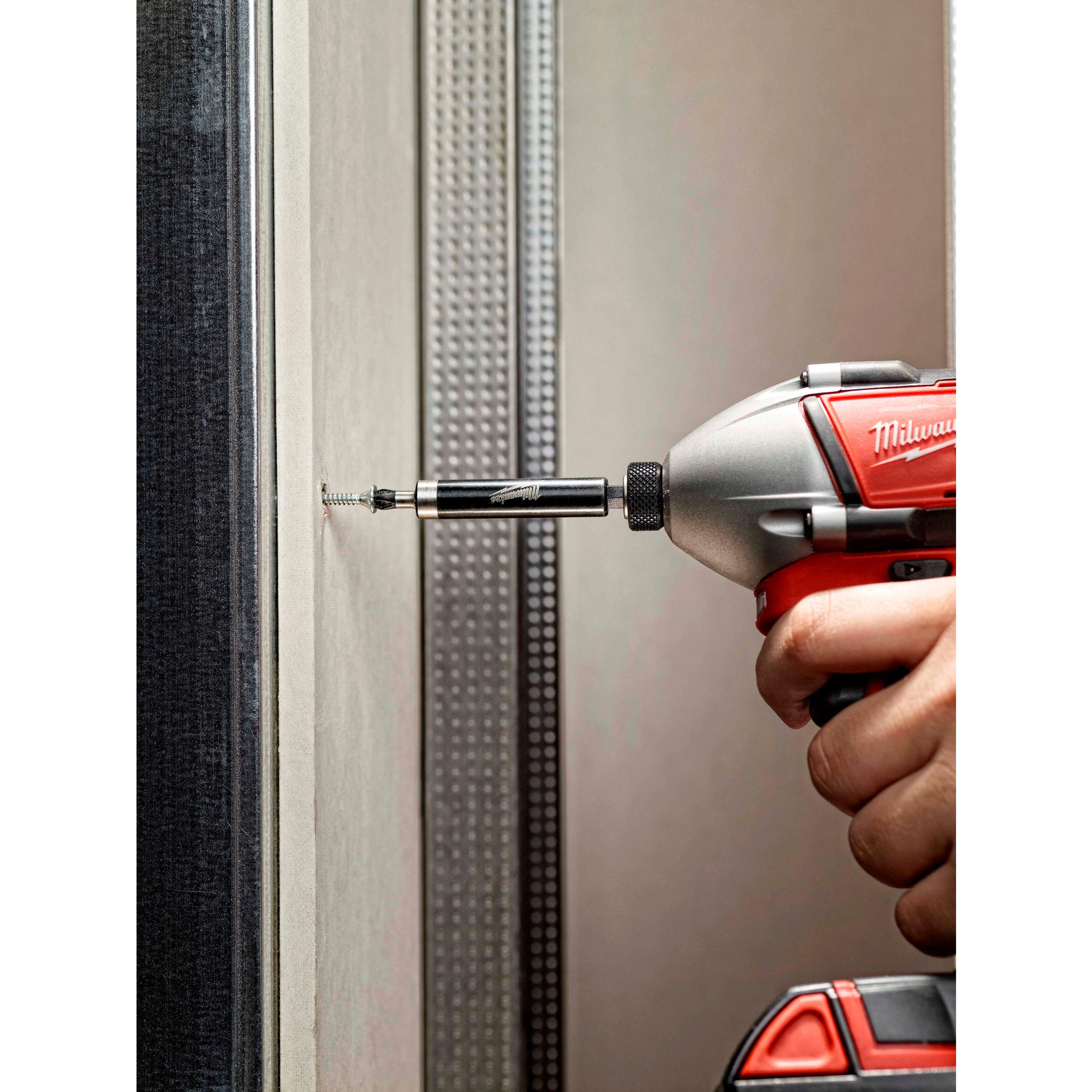 A power drill being used with a Magnetic Bit Holder to screw into a wall. The bit holder securely holds the screw in place.