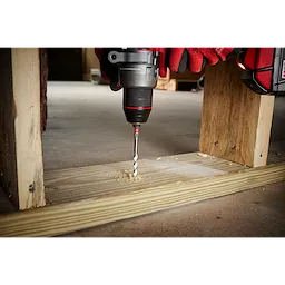 Handheld drill with 1/4" x 4" x 6" SHOCKWAVE Impact Duty Carbide Multi-Material Drill Bit drilling through a wooden plank.