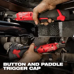 The image shows hands using the M12 FUEL™ 3/8" Ratchet in an automotive repair setting. The tool appears red and black, with a clear focus on its button and paddle trigger cap functionality.