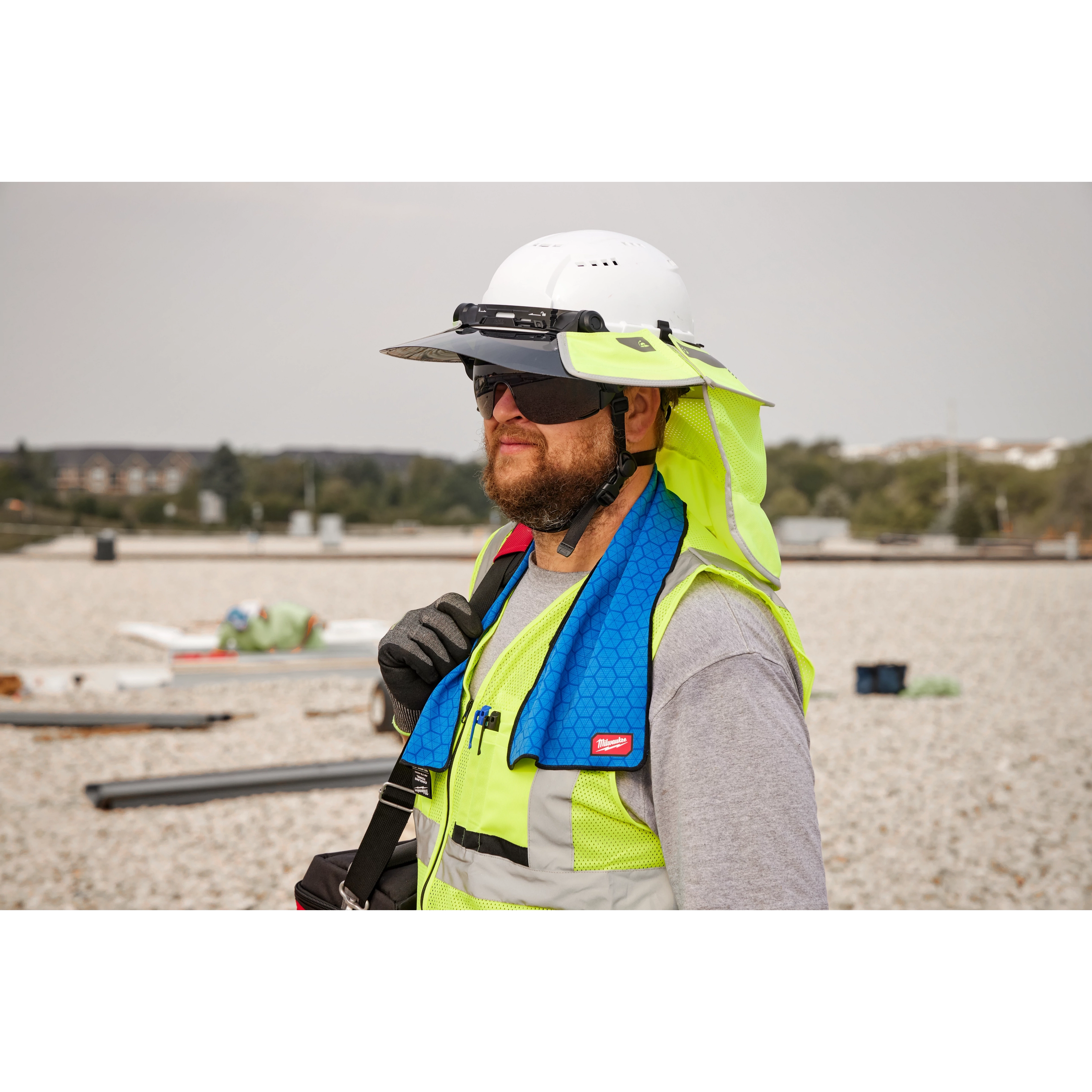 A construction worker wearing a high-visibility vest and hard hat, using a blue Cooling Towel around their neck on a job site.