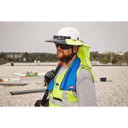 A construction worker wearing a high-visibility vest and hard hat, using a blue Cooling Towel around their neck on a job site.