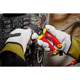 Gloved hands using a 1000V Insulated 10-20 AWG Wire Stripper & Cutter to strip wires inside an electrical panel.