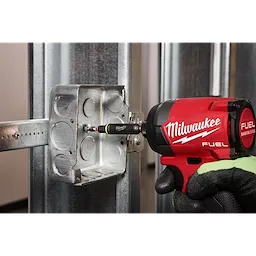 A worker is using the Milwaukee 8-IN-1 Multi-Bit & Nut Driver with SHOCKWAVE Impact Duty Bits & Nut Drivers to secure a metal electrical box to a steel stud. The tool is attached to a red Milwaukee FUEL cordless impact driver.