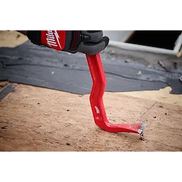 The 18" Wrecking Bar is shown being used to remove nails from a wooden surface. It is bright red with a chiseled end and is held by a hand wearing a Milwaukee-branded glove. The tool is bent for increased leverage and efficiency in demolition tasks.