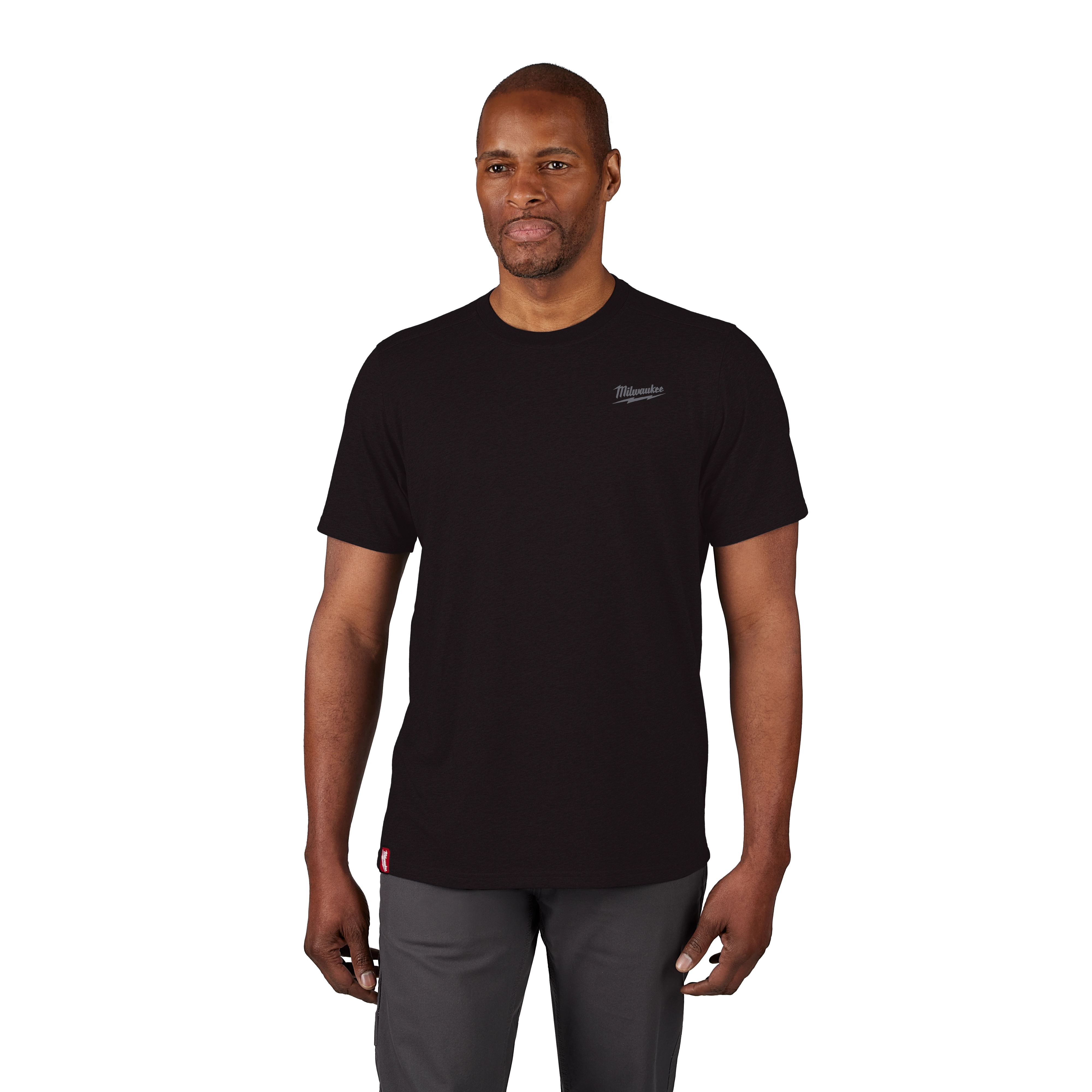 Man wearing a black Hybrid Work Tee with short sleeves, small logo on upper left chest, and red tag near hem, paired with gray pants.
