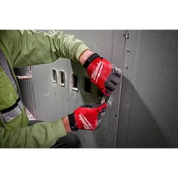 Person wearing Lightweight Work Gloves - L in red and black, working with electrical wires against a green drywall, wearing green shirt.