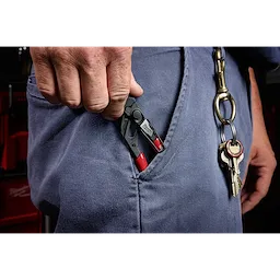 A person is placing a 5" Pliers Wrench with Belt Clip into the pocket of blue work pants. Keys clipped to a key ring are also visible on another belt loop.