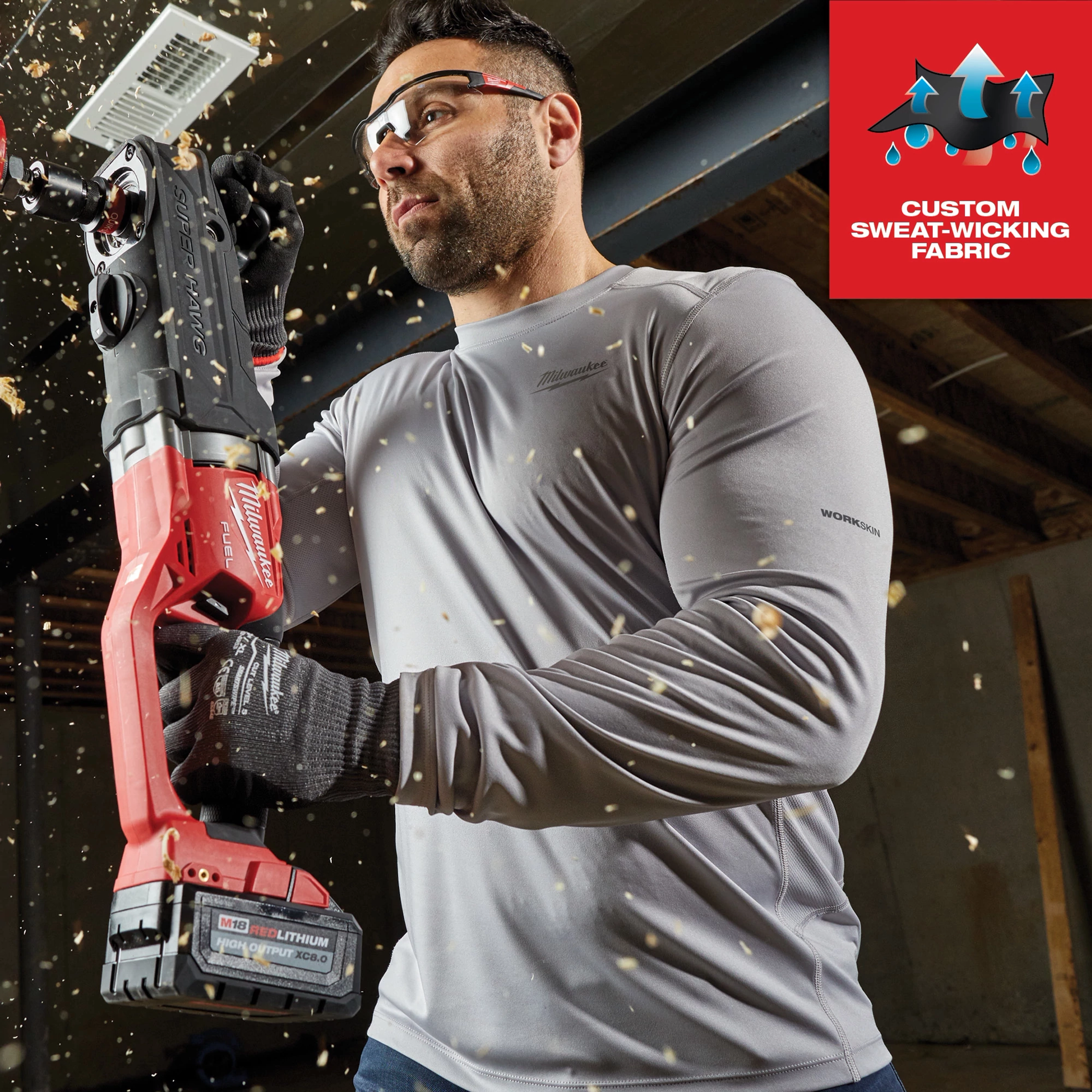 Person wearing WORKSKIN Lightweight Performance Shirt - Long Sleeve holding a power tool surrounded by wood shavings. Custom sweat-wicking fabric.