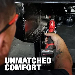 A person uses the M12 FUEL™ 1/2" Ratchet to tighten a bolt in a tight space. The tool is red and black, featuring the text "UNMATCHED COMFORT" in large white letters.