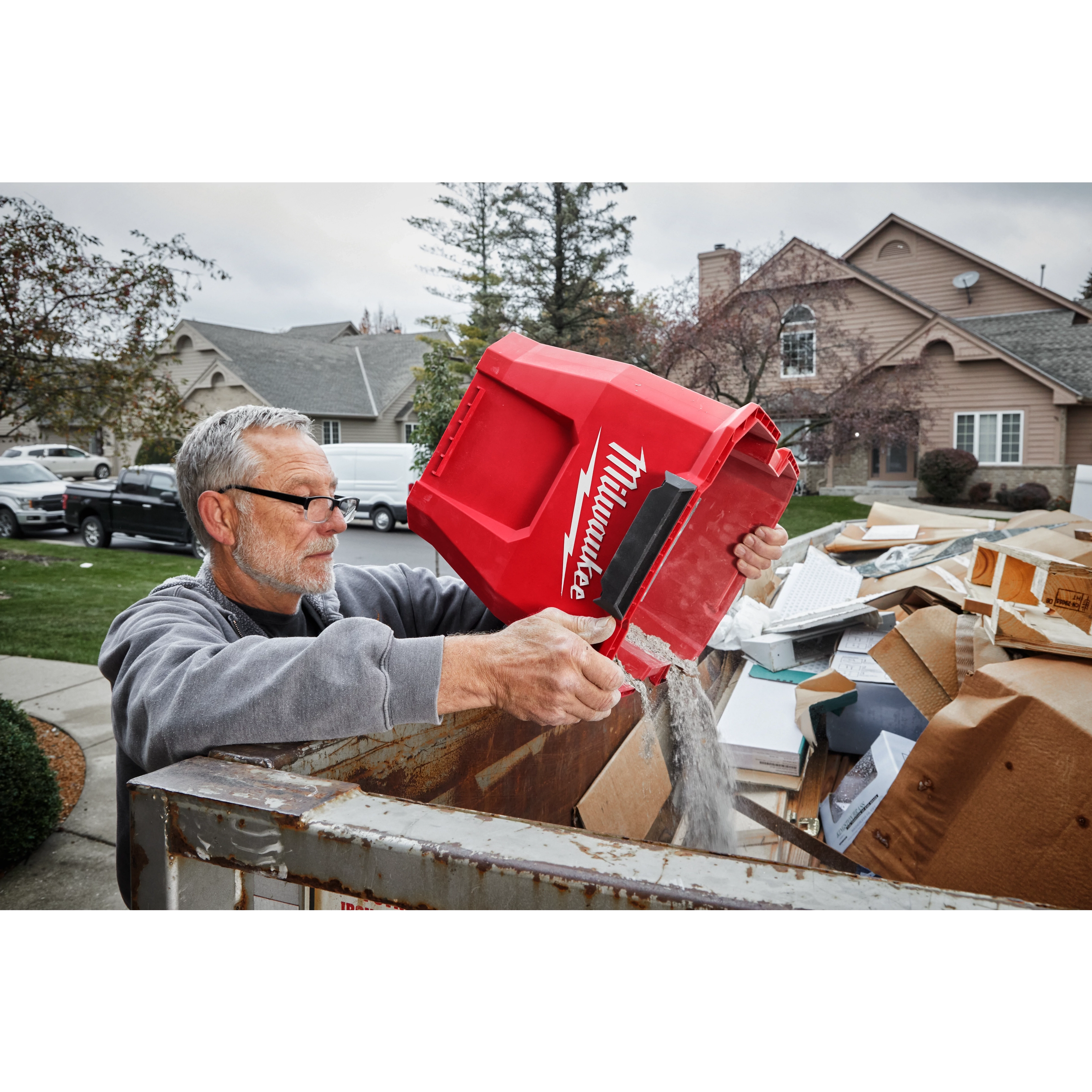A man empties debris from a 9 Gallon Wet/Dry Vacuum Tank into a large outdoor trash bin in a residential area.