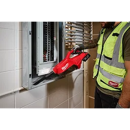 A worker uses the red M18 Brushless Handheld Vacuum to clean dust from an electrical panel. The vacuum is battery-operated and branded with the Milwaukee logo.