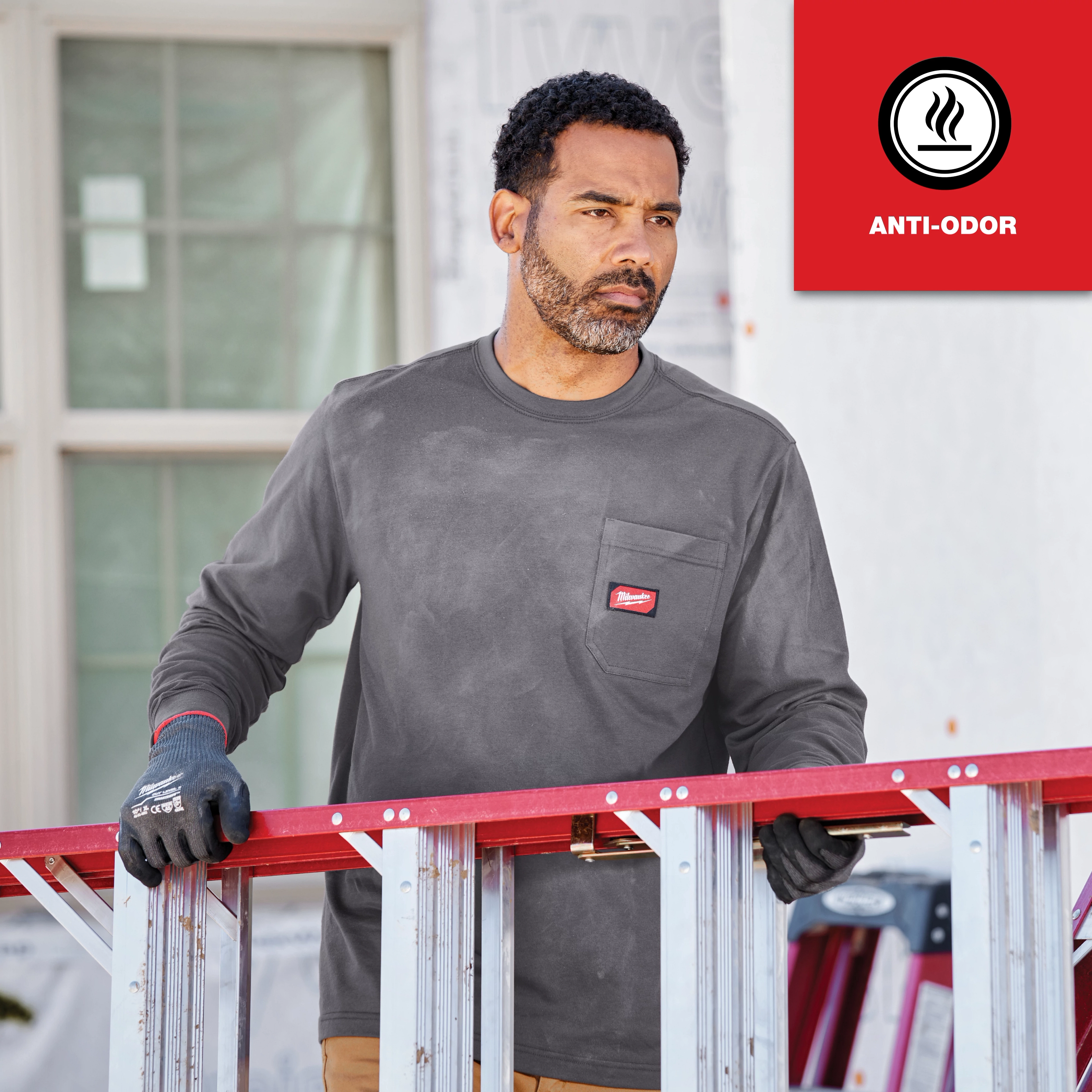 Person wearing GRIDIRON Pocket T-Shirt - Long Sleeve Anti-Odor, holding a red and silver ladder, standing outside a building.