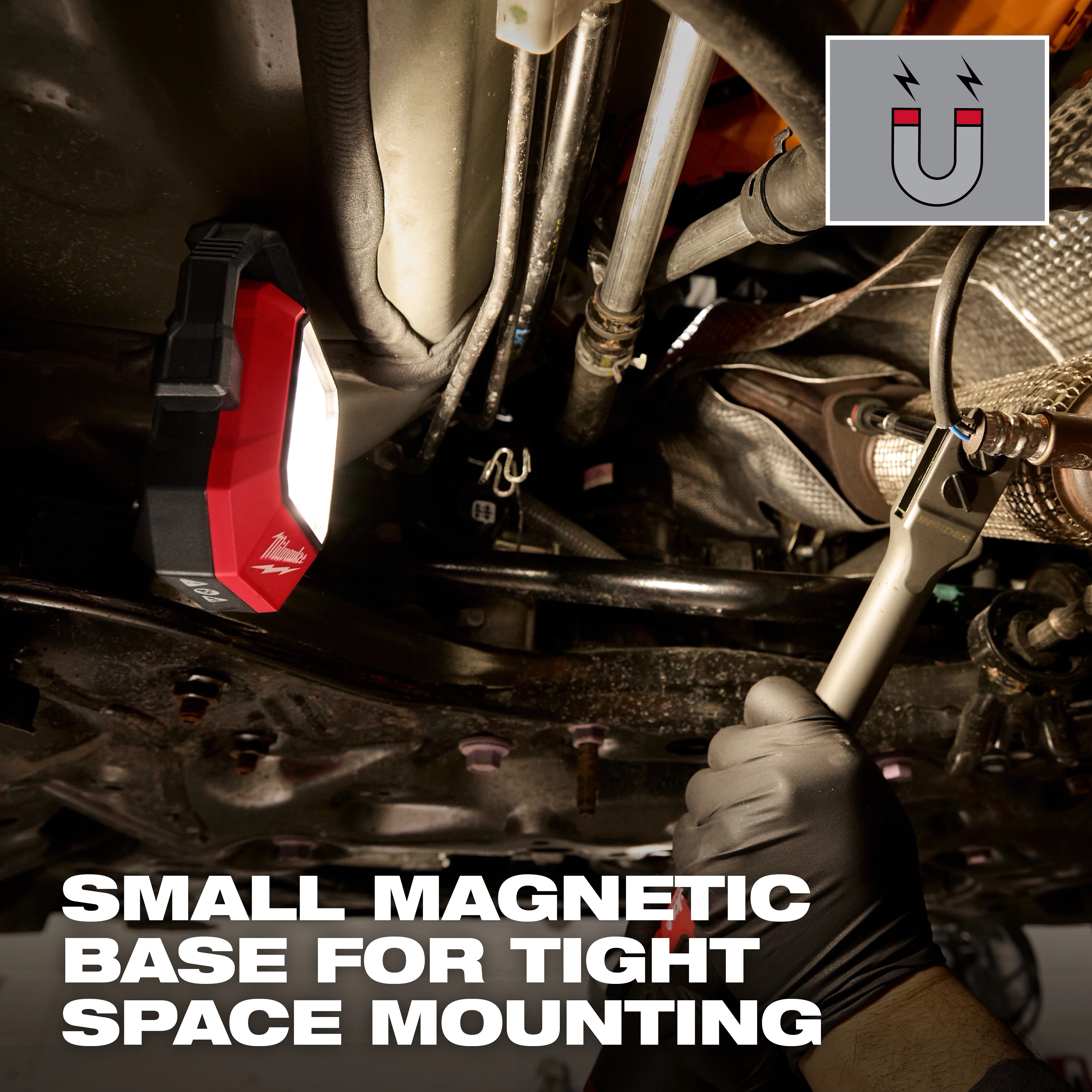Milwaukee Rechargeable Pivoting Task Light w/ Spot Mode magnetically mounted under a vehicle as a gloved hand uses a wrench.