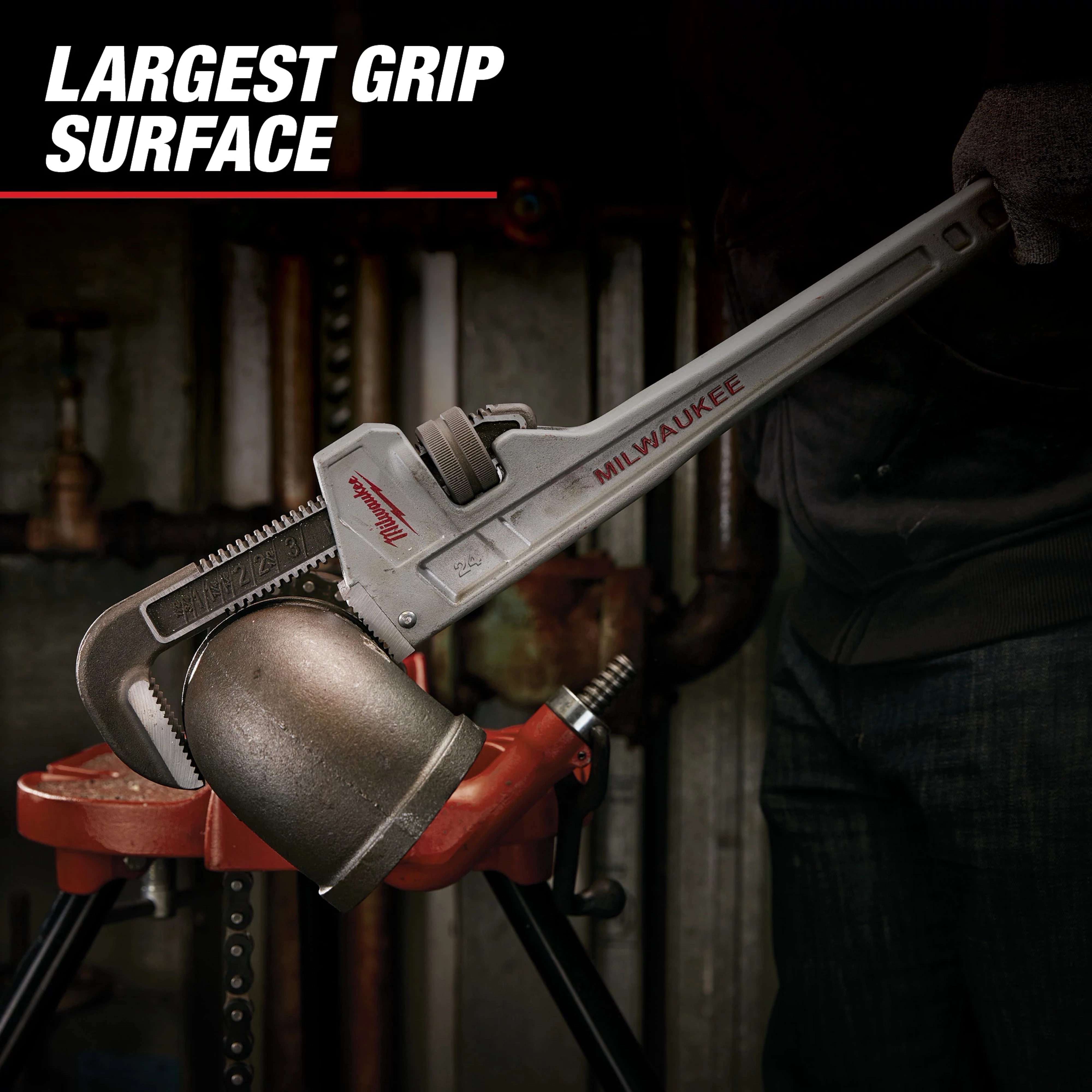 Milwaukee Steel Pipe Wrench in use, clamped onto a large pipe fitting held by a red vise. The message "Largest Grip Surface" is displayed at the top left.