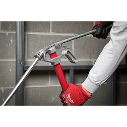 Person using 1/2" EMT Aluminum Conduit Bender with red handle to bend a metal conduit against a gray brick wall.