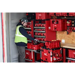 Worker organizing PACKOUT Low-Profile Crate, PACKOUT Compact Crate, and PACKOUT XL Crate in a storage unit equipped with shelving.
