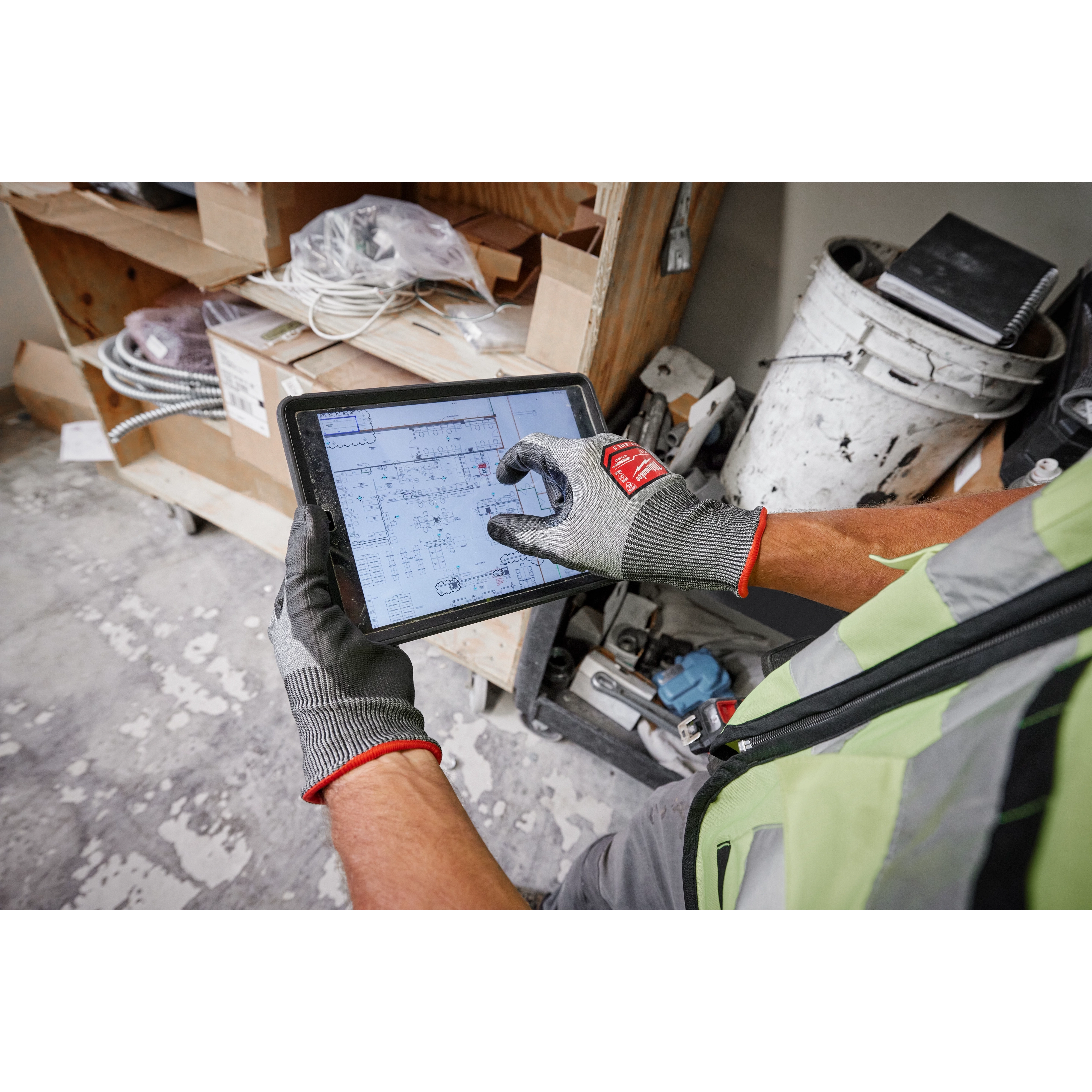 Person wearing Cut Level 5 High Dexterity Polyurethane Dipped Gloves - L while using a tablet to view a floor plan in a workshop.