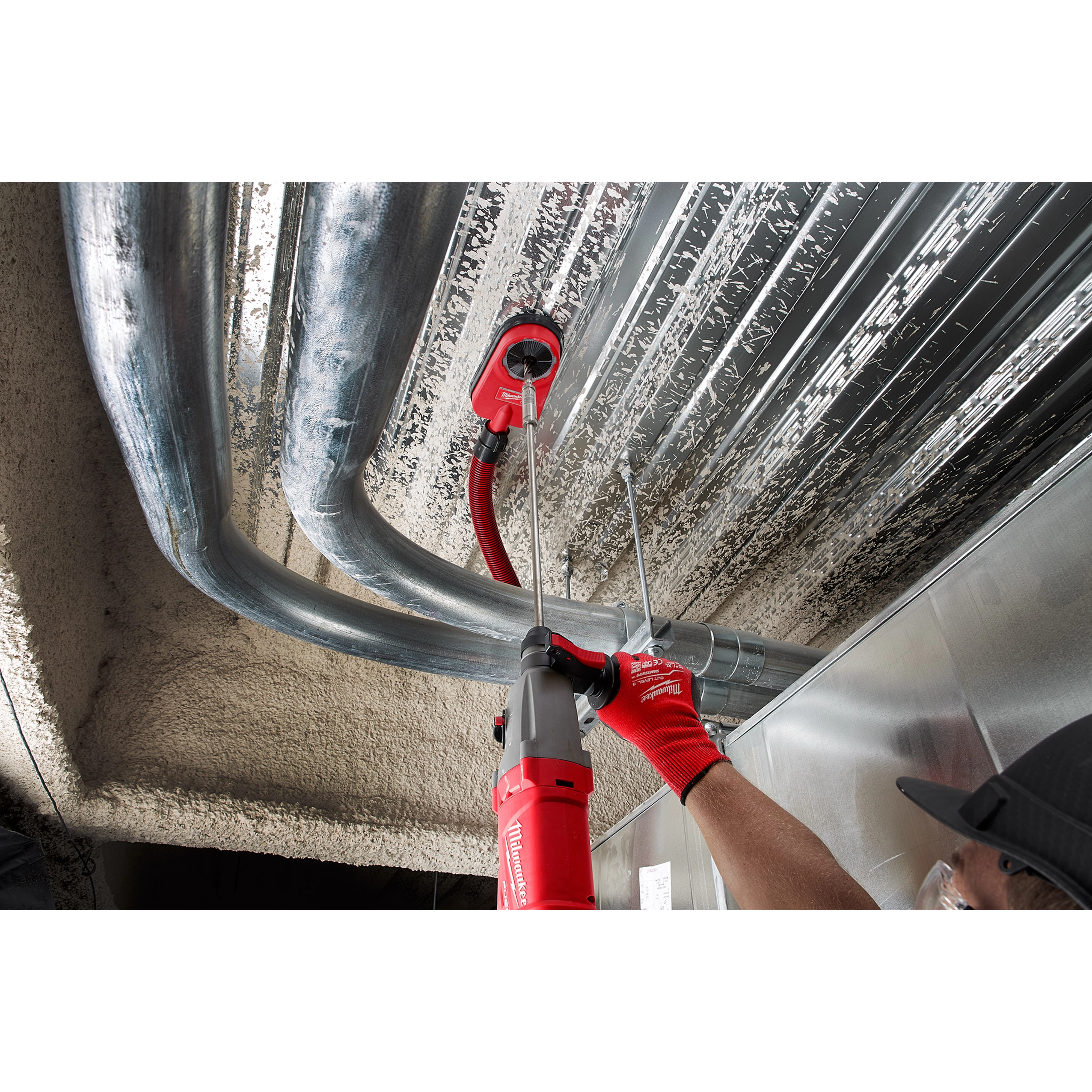 A worker uses an SDS PLUS 18” EXTENSION with a red power drill to install piping in a ceiling, wearing red gloves and a black cap.