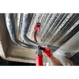 A worker uses an SDS PLUS 18” EXTENSION with a red power drill to install piping in a ceiling, wearing red gloves and a black cap.