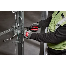 A person using the 10-24 AWG Compact Dipped Grip Wire Stripper & Cutter to strip and cut wires attached to a metal frame. The person is wearing gloves and a safety vest.