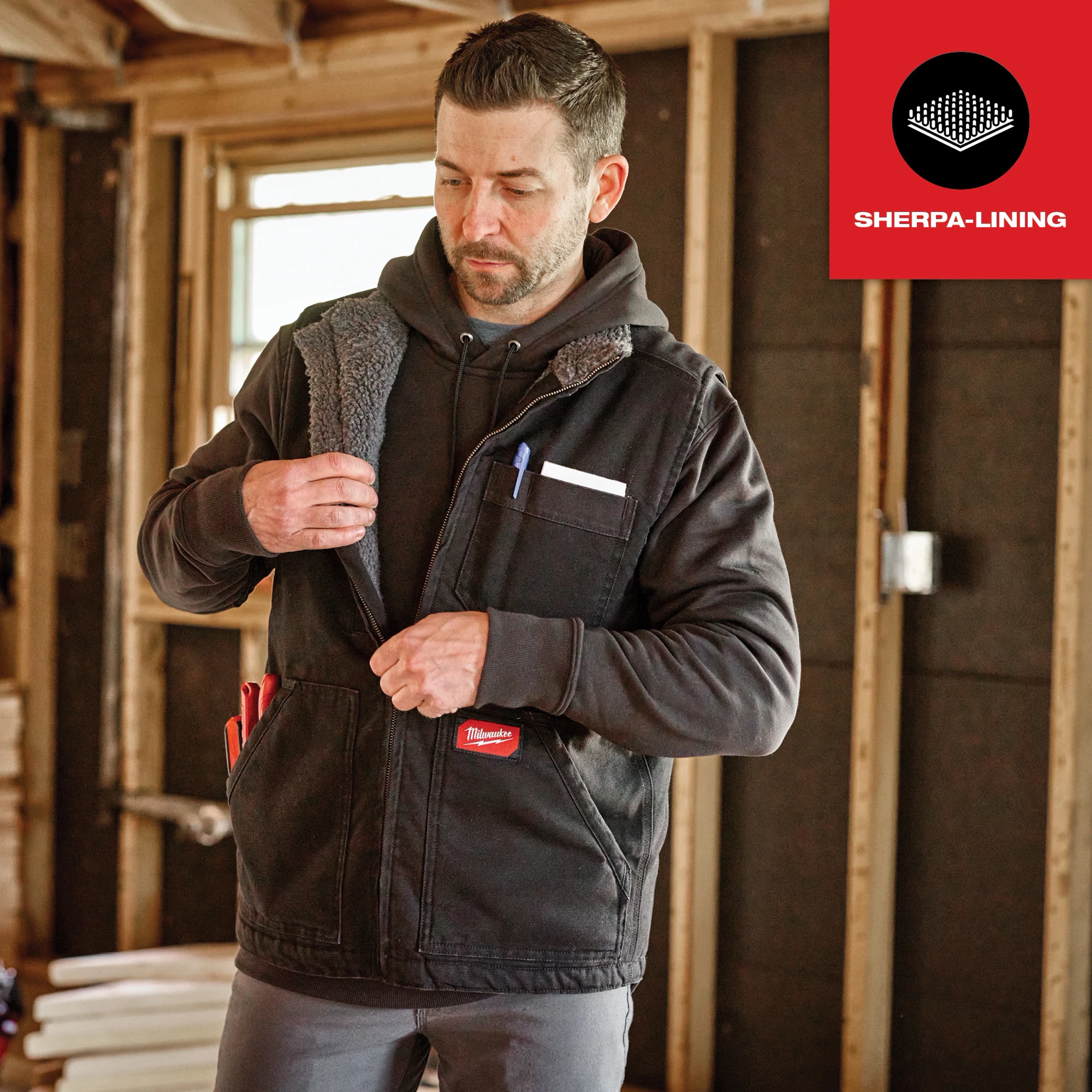 Heavy Duty Sherpa-Lined Vest Feature Shot, in black, worn by a person in a construction setting with various tools in vest pockets.