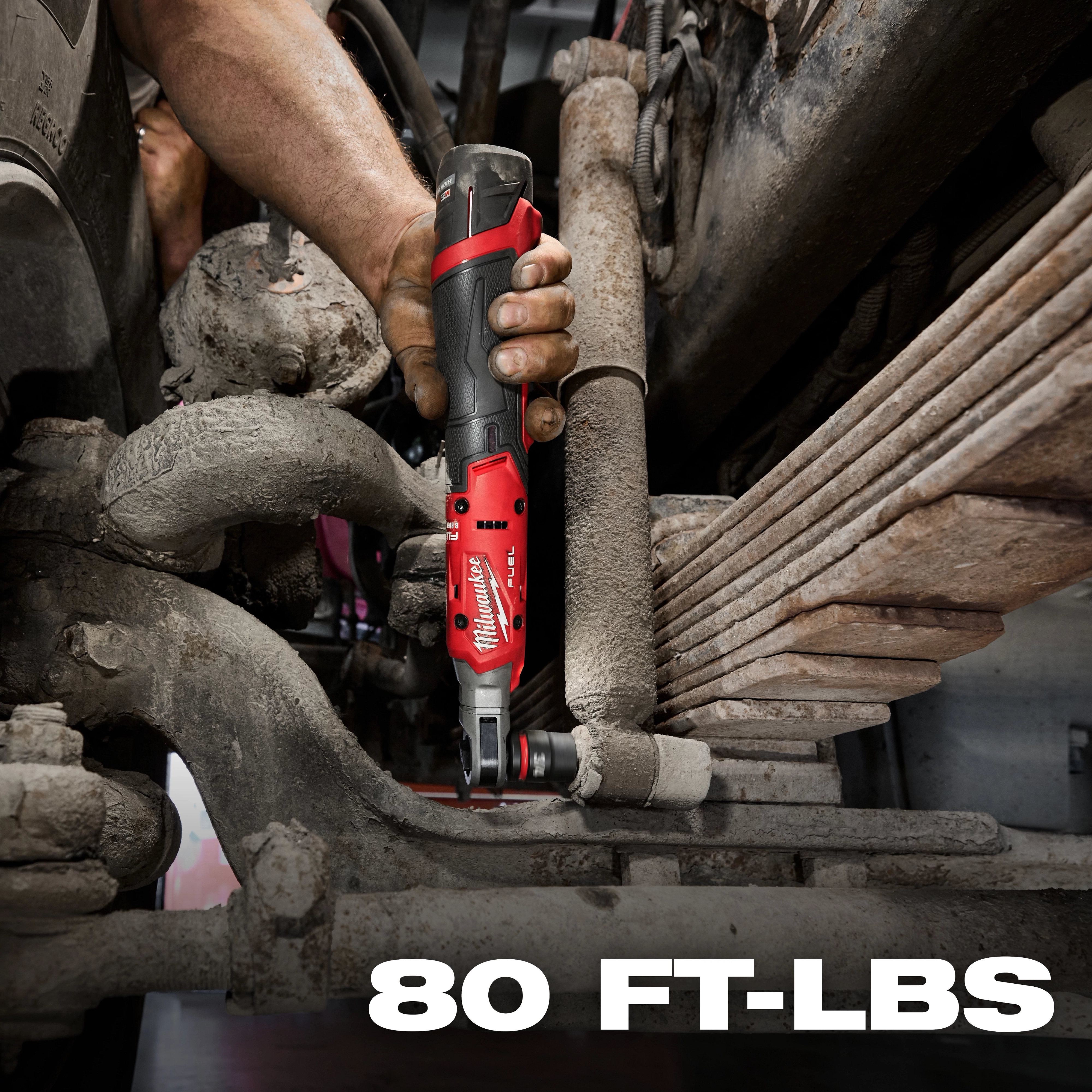 A person is using the M12 FUEL™ 1/2" Ratchet to tighten a bolt in a dirty, tight mechanical environment. The product features a black and red design and operates with a torque power of 80 foot-pounds, as indicated by text in the bottom right corner.