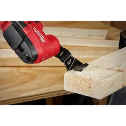 MILWAUKEE OPEN-LOK 2-1/2" HCS Wood Multi-Tool Blade attached to a red tool, actively cutting through a wooden beam.
