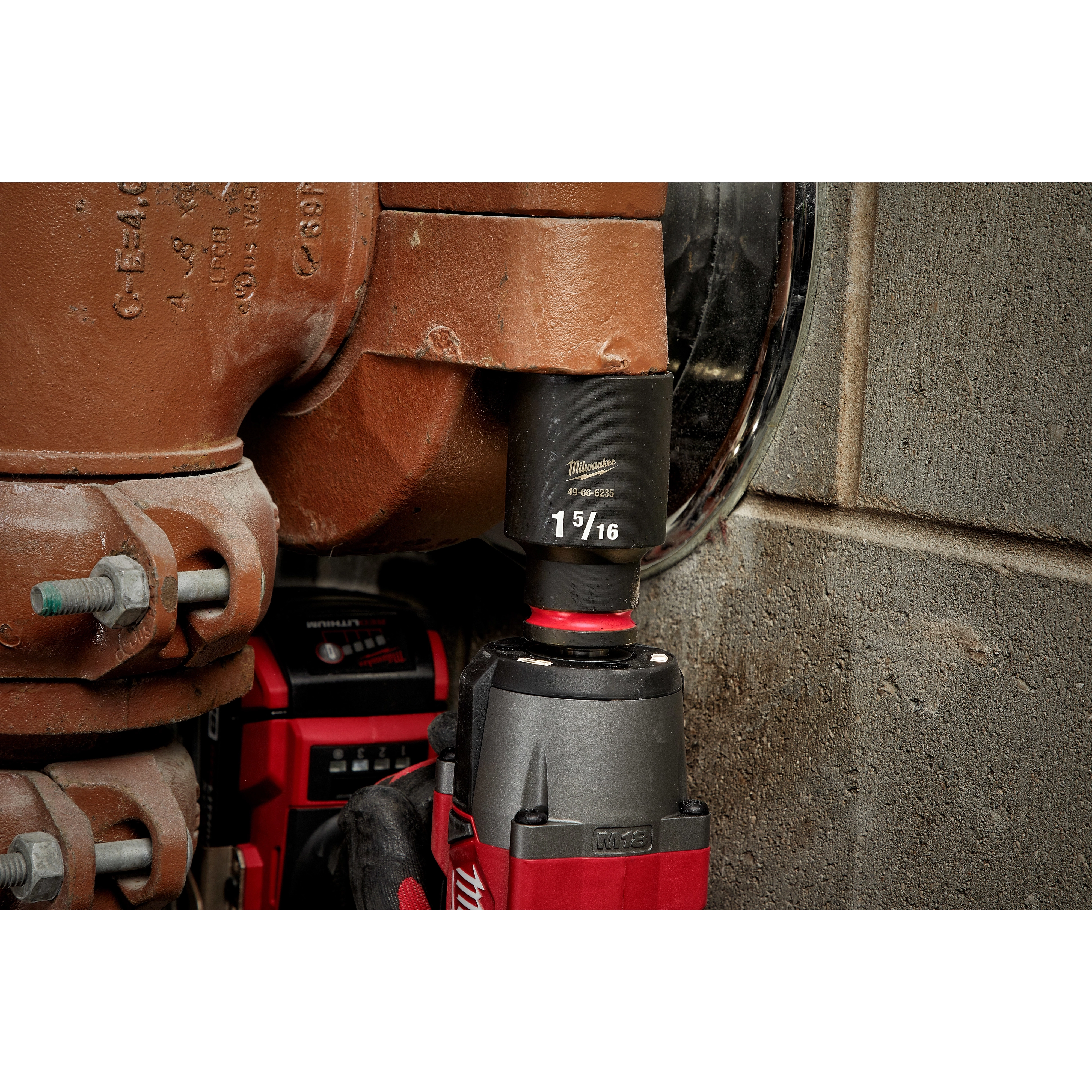 The SHOCKWAVE%20Impact%20Duty%E2%84%A2%201%2F2%22%20Drive%201-5%2F16%22%20Deep%206%20Point%20Socket is attached to a power tool, being utilized to tighten a large bolt on an industrial pipe fitting. The socket is black and labeled with size 1-5/16".